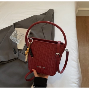 Detail of dark red woven bucket bag with beaded charm and gold metallic brand plate