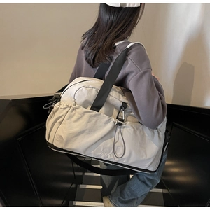 Detailed view of beige travel tote featuring side drawstring pocket and black straps
