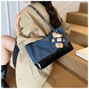 Detail of denim and patent leather tote bag featuring a cute teddy bear charm