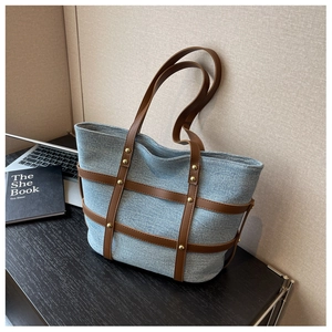 Detail of denim tote bag with brown leather cage frame and gold rivet accents
