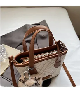 Detail of checkered Boston tote with brown handles and plush bow charm on a table