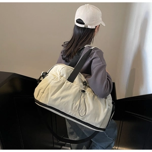 Detail of off-white pleated travel bag with black strap and bottom expansion zipper