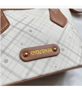 Close-up of checkerboard pattern with brown leather label and golden rivets on tote bag