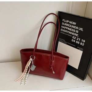 Detail of burgundy leather tote bag featuring a tennis racket charm and embossed logo
