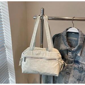 Close-up of a cream nylon shoulder bag featuring a front zipper pocket and side drawstrings