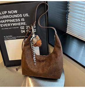 Detail of dark brown suede hobo bag with teddy bear charm on a metal table