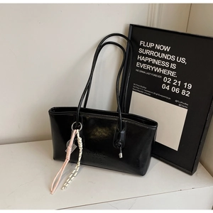 Close-up of black glossy leather tote bag featuring debossed fashion logo and woven charms