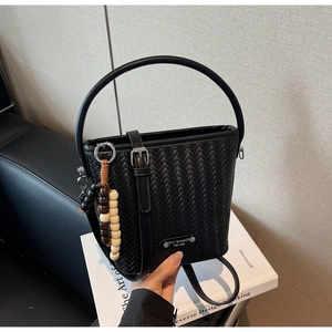 Detail of black woven texture bucket bag with wooden bead charm and adjustable leather strap