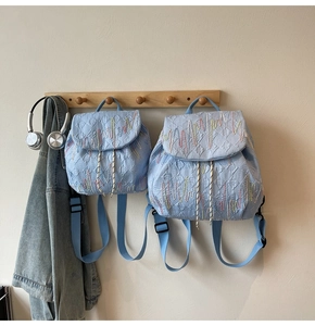Detail of light blue textured backpacks with wavy embroidery and drawstring closure
