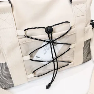 Detail of beige travel tote featuring transparent PVC pocket and black elastic bungee cord