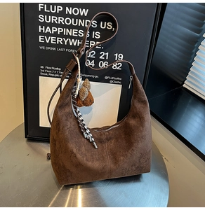 Brown suede crescent bag detail with plaid scarf and cute bear charm on a silver surface