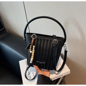 Detail of black woven bucket bag with wood bead charm and rounded leather handle