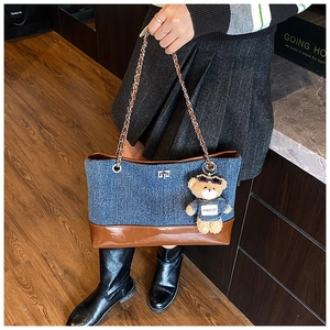 Detail of denim tote bag featuring brown leather trim and a cute plush bear charm