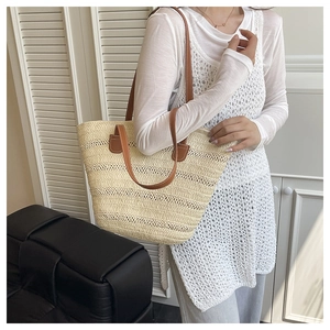Close-up of beige woven tote bag with brown leather handles worn by a model