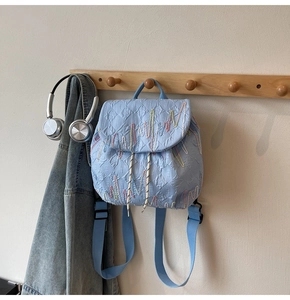 Detail of light blue quilted backpack featuring colorful wavy embroidery and white drawstring