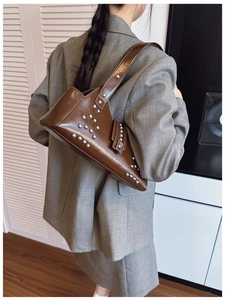 Brown leather underarm bag with silver rivets shown on a model in a grey suit