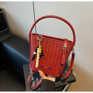 Close-up of red woven texture bucket bag with beaded tassel and metal logo detail