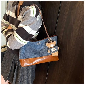 Detail of denim and leather contrast tote bag with metal chain and plush bear charm