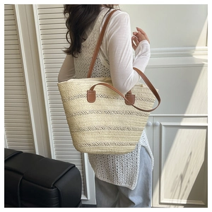 Close-up of a woven straw tote bag with brown leather handles and textured ivory finish