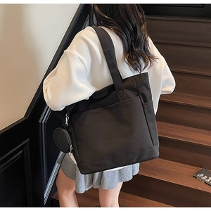 Detail of black canvas tote bag with side pocket, circular coin pouch and large front pocket