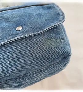 Macro shot of blue denim fabric texture and silver metal button on a small square bag