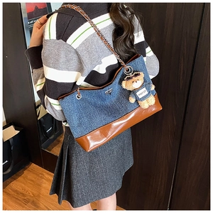 Detailed side view of large denim tote bag with leather trim and gold chain strap