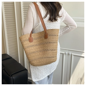 Detail of woven straw tote bag featuring brown leather shoulder straps and precise stitching