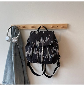 Quilted black backpack featuring colorful wave embroidery on light beige wall background