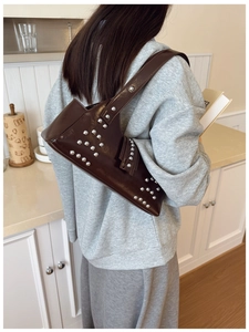 Detail view of coffee brown patent leather underarm bag with silver metallic rivets