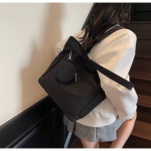 Detail of black nylon tote bag and detachable round pouch carried by a model on stairs