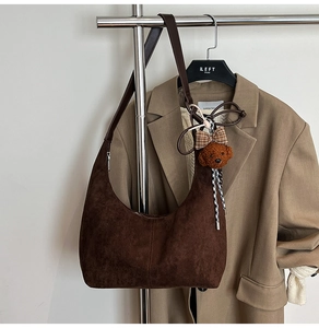 Detail of dark brown suede hobo bag with teddy bear charm against khaki blazer background