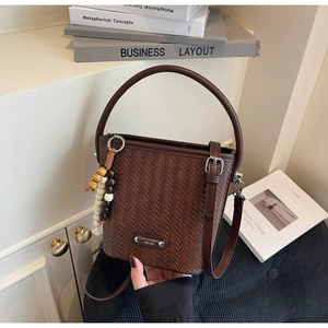 Detail of dark brown woven texture bucket bag with wooden bead charm and metal plaque
