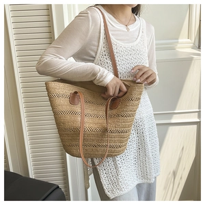 Straw tote bag with brown leather straps shown against a clean white interior background