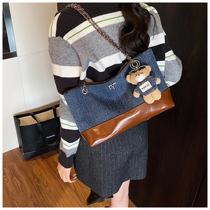 Detail of denim tote bag with leather patchwork, chain strap and teddy bear charm