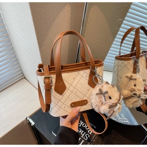 Detail of checkered tote bag with plush bunny charm and adjustable brown leather strap