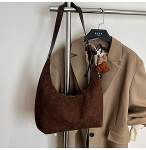 Close-up of a brown suede hobo bag with a cute bear plush charm and khaki blazer background