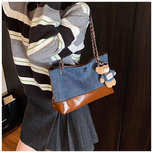Detail of color-block denim tote with silver chain and a teddy bear charm on model