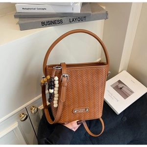 Detailed view of brown woven bucket bag with wood bead charm and adjustable strap