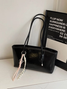Large black glossy leather tote bag with shoulder strap and pink knot accessory