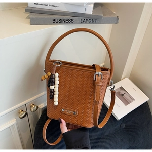 Close-up of brown woven bucket bag with wood bead tassel and metal logo detail