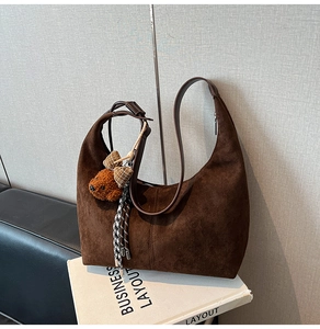 Detail of dark brown suede hobo bag featuring a cute teddy bear charm and leather strap