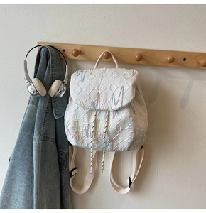 Detailed view of quilted white backpack with colorful letter embroidery and drawstring