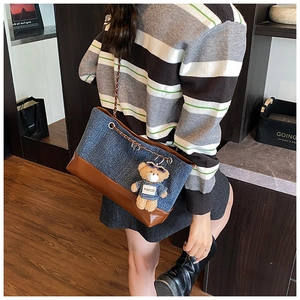 Detail of denim tote bag with brown leather base and teddy bear charm on chain strap