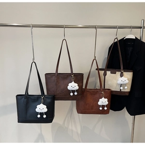 Close-up of four colored faux leather tote bags with cloud pendants hanging on a rack