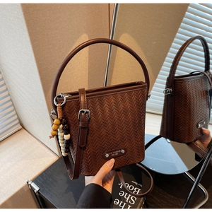 Detail of dark brown woven bucket bag with wood bead charm and metallic logo plate