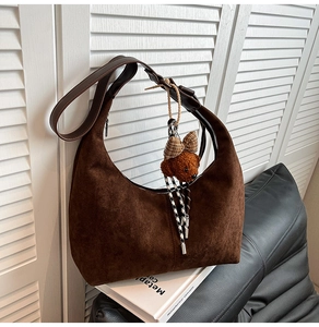 Close-up of brown suede crescent bag with a cute teddy bear charm on white shutters