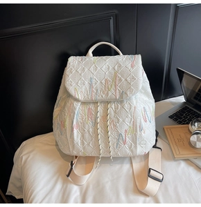 Detailed macro view of quilted white backpack with colorful embroidery and woven straps