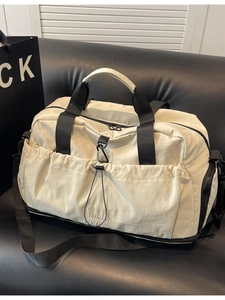 Large beige travel duffel bag with black straps on a leather sofa for sport and gym use