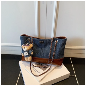 Detail of denim tote bag with leather trim, silver chain, and denim bear charm