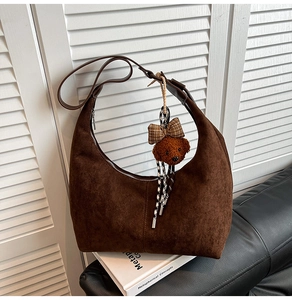 Detail of dark brown suede hobo bag with teddy bear charm on a classic leather sofa